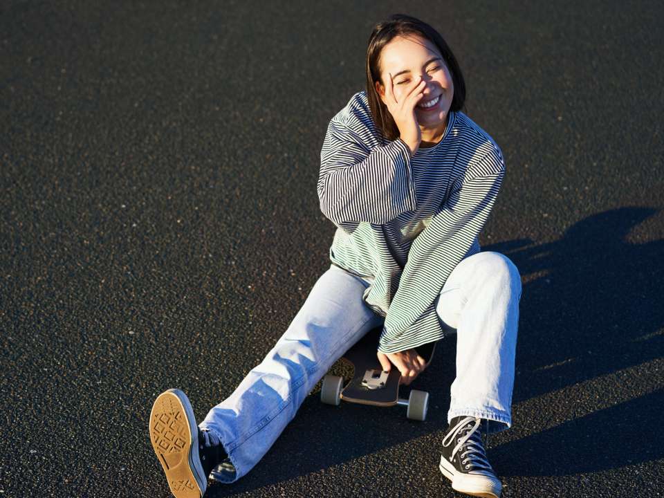 A woman laughs after falling off a skateboard.