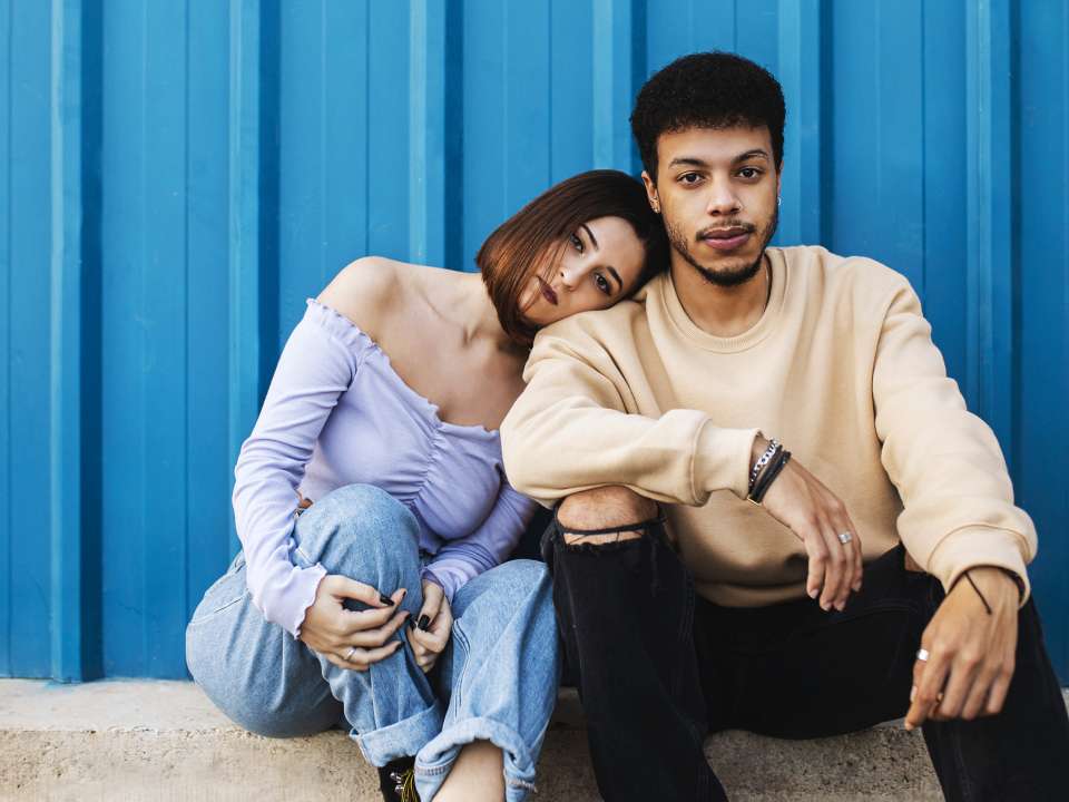 A man and woman sit in front of a blue background.